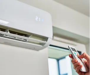 Main tenant une télécommande d'air conditionné, avec une unité de climatisation murale blanche allumée à Buxières-d'Aillac près de Châteauroux dans l'Indre 36