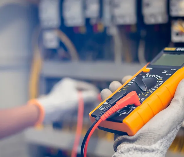 Électricien en gants mesurant la tension avec un multimètre dans un panneau électrique à Buxières-d'Aillac près de Châteauroux dans l'Indre 36
