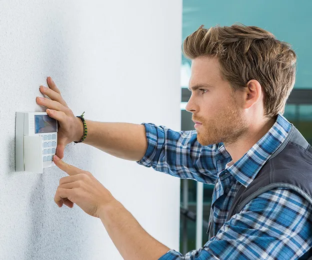 Homme barbu en chemise à carreaux bleue, installant un système d'alarme sur un mur blanc à Buxières-d'Aillac près de Châteauroux dans l'Indre 36