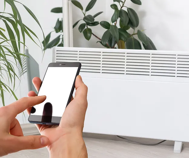 Personne contrôlant un chauffage électrique blanc avec un smartphone à Buxières-d’Aillac près de Châteauroux dans l'Indre 36